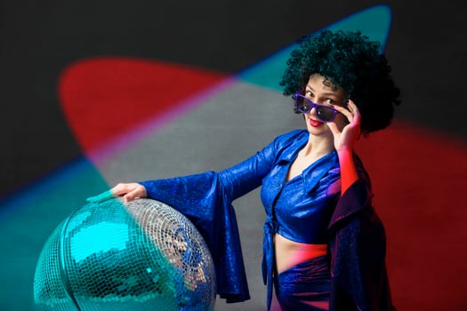 A woman with a disco ball in an afro wig in multi-colored rays of light. Disco style from the seventies or eighties. photo