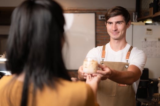 Barista holding a glass of cold latte coffee in his hands to customer photo