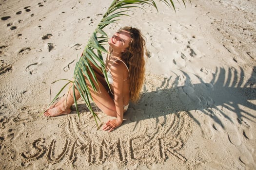 young skinny woman in white bikini swimwear holding leaf of palm tree photo
