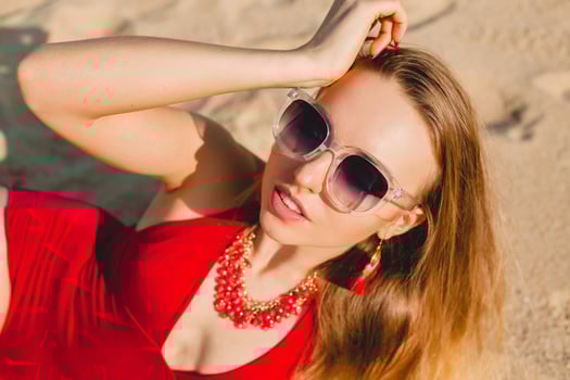 young beautiful blond woman sunbathing on sand beach in red swimming suit, sunglasses photo