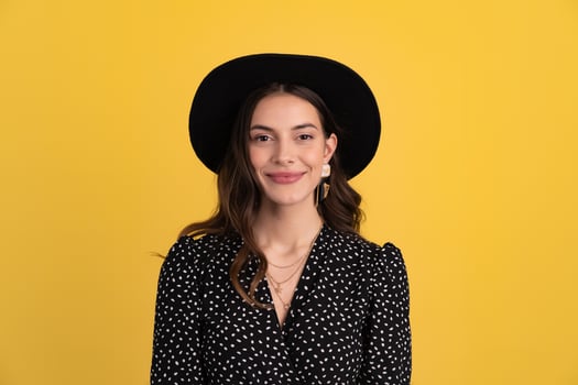 attractive woman posing isolated on yellow background wearing black hat and dress photo