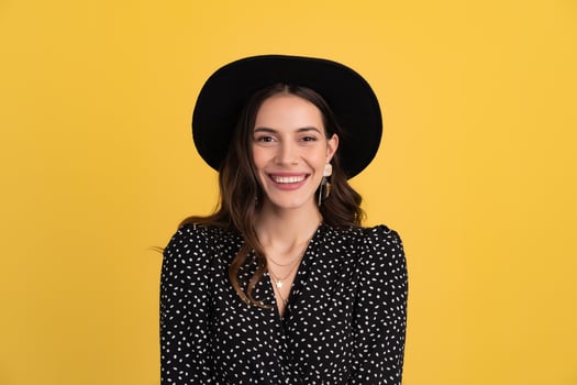 attractive woman posing isolated on yellow background wearing black hat and dress photo