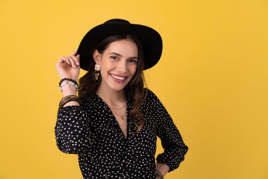 attractive woman posing isolated on yellow background wearing black hat and dress photo