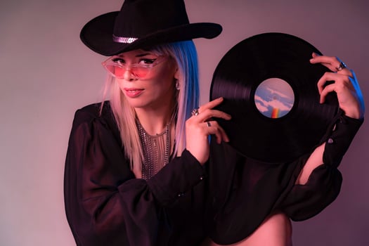 Sexy Dj woman looks over colored glasses holding a vinyl record with a black hat. photo