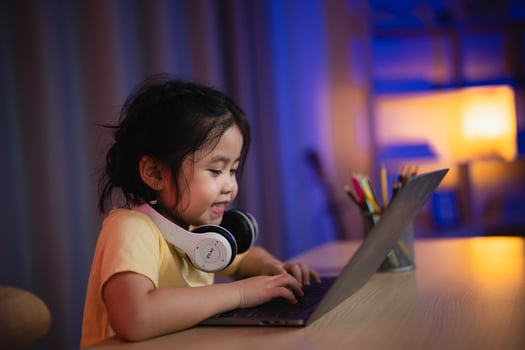 Asian girl smiling, laughing, excited, looking, wearing white headphone and using laptop streaming night light in living room at home. Cute girl watching videos while tv Internet addiction concept. photo