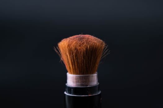 Cosmetic brush with pastel pink cosmetic powder spread on black background. Makeup brush with pink powder explosion close up. photo