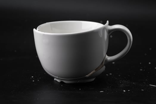 Large white mug with cracks. White cup for tea or soup with cracks isolated on dark background. Broken ceramic cup close up. symbol of divorce or loss photo