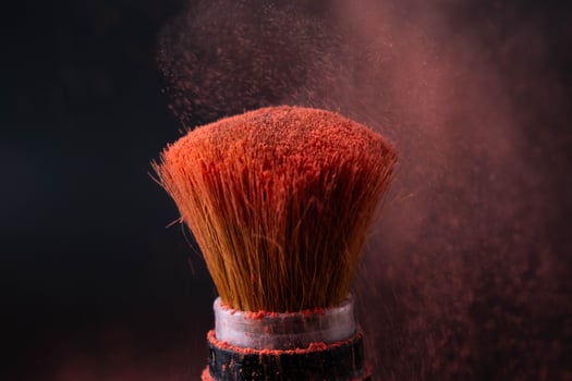 Cosmetic brush with pastel pink cosmetic powder spread on black background. Makeup brush with pink powder explosion close up. photo