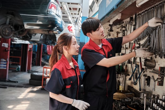 Two professional Asian mechanic partners discuss hand tools and machinery for fixing work at car service garage, maintenance jobs, and check and repair occupation in automotive industry business. photo