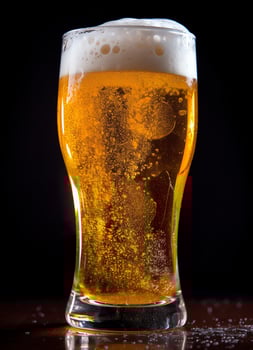 A glass of cold fresh beer with cap of foam. Splash of foam with tasty american beer. Beer day concept by AI Generated photo