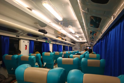 Executive class train interior with blue seats, armrests, luggage racks, monitor screens, air conditioning, and lights that extend on the ceiling photo