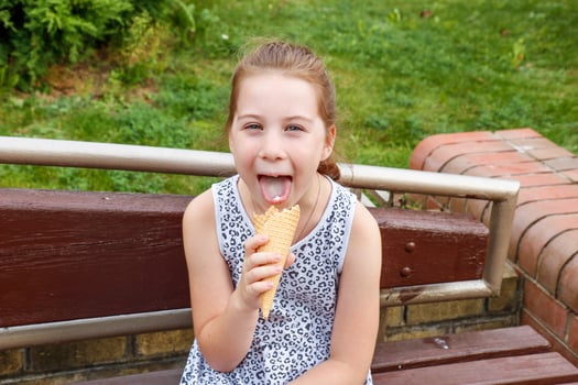 funny girl licks ice cream while sitting on a park bench photo