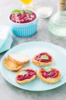 Homemade bruschetta with beetroot hummus on small baked baguette toast on a plate and a bowl of hummus on the table. Vertical view photo