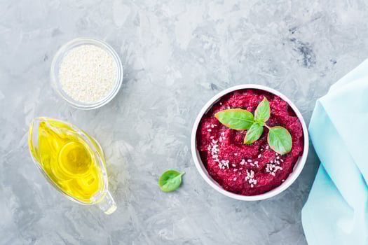 Homemade baked beetroot hummus in a bowl with sesame seeds and basil on the table. Top view photo