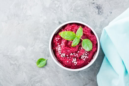 Homemade baked beetroot hummus in a bowl with sesame seeds and basil on the table. Close-up. Top view photo