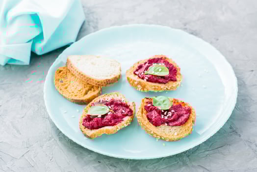Homemade bruschetta with beetroot hummus on small baked baguette toast on a plate on the table. Close-up photo
