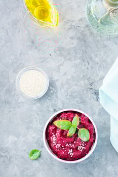 Homemade baked beetroot hummus in a bowl with sesame seeds and basil on the table. Top and vertical view photo