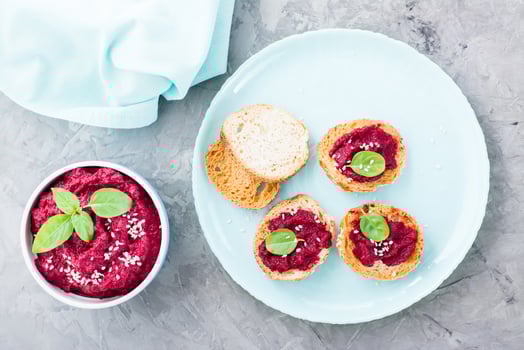 Homemade bruschetta with beetroot hummus on small baked baguette toast on a plate and a bowl of hummus on the table. Top view photo