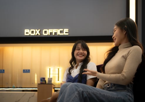 Two young asian women eating popcorn and waiting for watching movie at front of box office photo