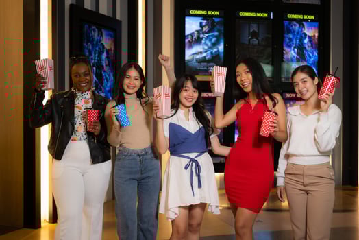 Group of happy friends watching movie in cinema and eating popcorn at night photo