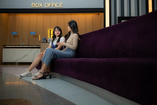 Two young asian women eating popcorn and waiting for watching movie at front of box office photo