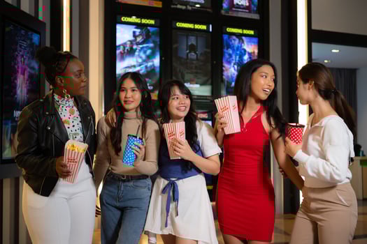 Group of happy friends watching movie in cinema and eating popcorn at night photo