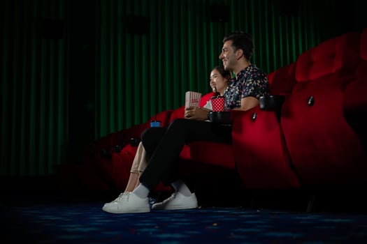 Young man and woman watching movie in cinema, sitting on red seats photo