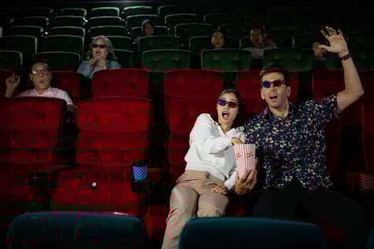 In a cinema, A young couple pair wearing 3D glasses watches movies and eats popcorn. photo