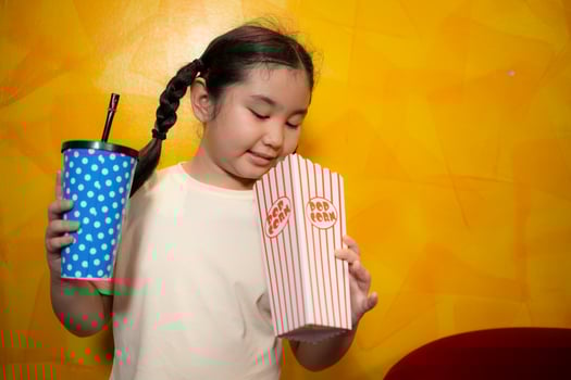Asian child girl eating popcorn and drinking soda on yellow wall background, Cinema concept, photo