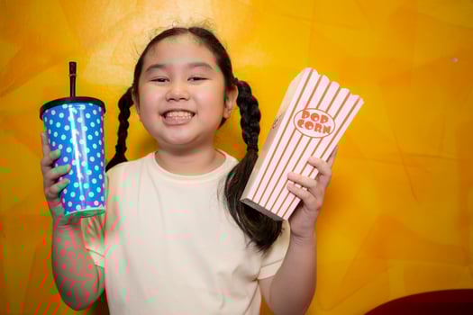 Asian child girl eating popcorn and drinking soda on yellow wall background, Cinema concept, photo