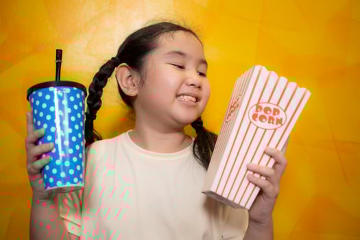 Asian child girl eating popcorn and drinking soda on yellow wall background, Cinema concept, photo
