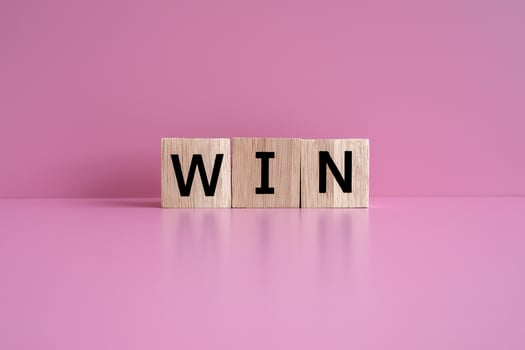 Wooden blocks form the text WIN against a pink background. photo