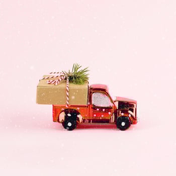 Red toy car delivering Christmas or New Year gift present box on pink background. photo