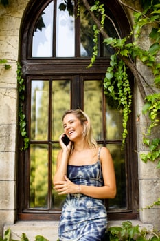 Pretty young woman using mobile phone by the old house with ivy photo