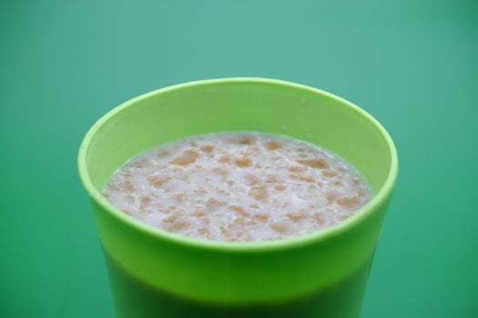 Green plastic cup containing cereal drink isolated on green background photo
