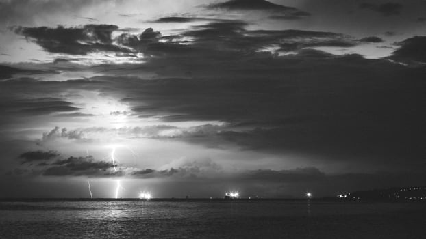 Epic photo of the sky over the sea with lightning in the clouds. Spectacular nature show. Long exposure photography, night landscape in black and white