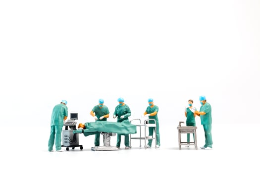Miniature Doctor performing surgery on patient on white background photo