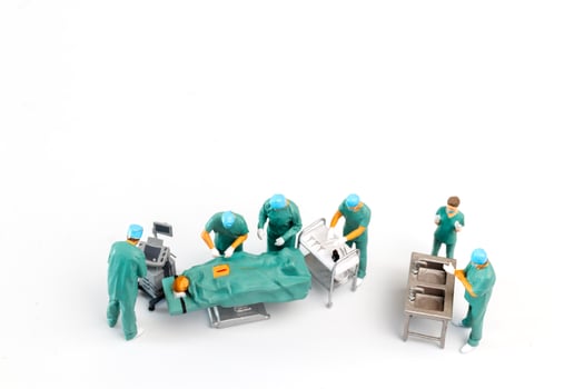 Miniature Doctor performing surgery on patient on white background photo