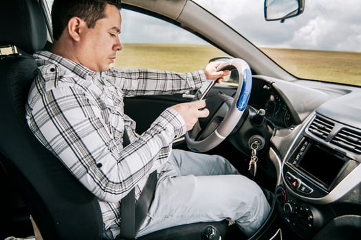 Man sitting in his car texting with his cell phone, Side view of a young man sitting inside car using mobile phone, Young man sitting in a car and looking at a mobile phone photo
