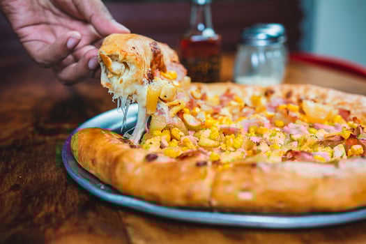 Hand taking a slice of ham and sweetcorn pizza. Homemade ham pizza with cheese and sweet corn served on wooden table photo