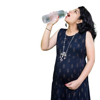 A pregnant Indian lady poses for pregnancy shoot and hands on belly with white background, Indian pregnant woman puts her hand on her stomach in maternity dress with plain background, Pregnancy shoot photo
