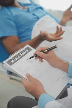 Close up of doctor sitting on bedside of male patient in hospital photo