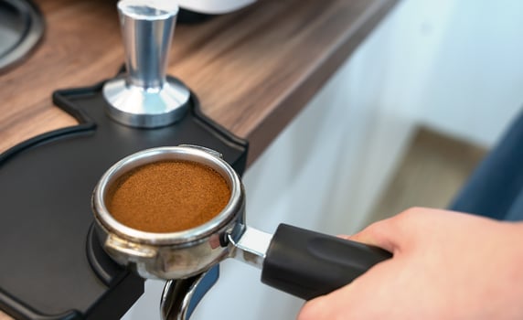 The barista's hand holds a holder with ground fresh coffee for making coffee in a coffee machine. Close-up. Selective focus. photo