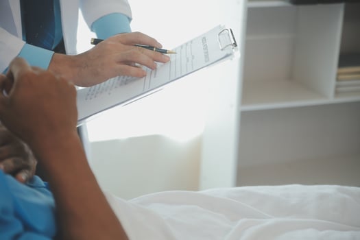 Close up of doctor sitting on bedside of male patient in hospital photo