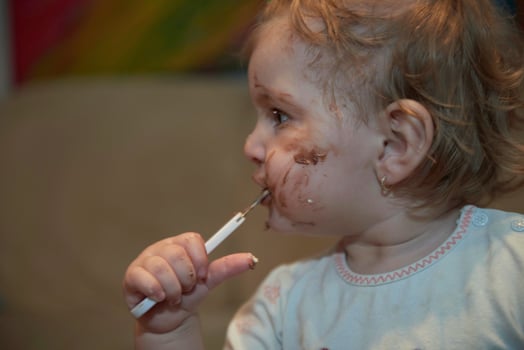 baby girl eating her chocolate desert with a spoon and making a mess photo