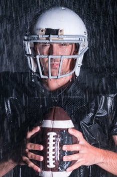 American Football Field Lonely Athlete Warrior Standing on a Field Holds his Helmet and Ready to Play. Player Preparing to Run, Attack and Score Touchdown. Rainy Night with Dramatic Fog, Blue Light photo