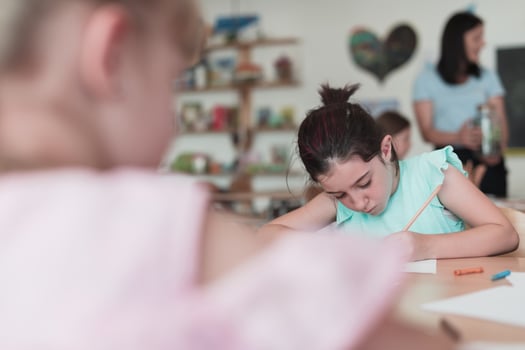 Little girls sitting in elementary school drawing on paper with their friends while sitting in a modern classroom photo