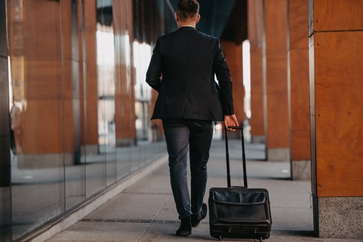 Going to airport terminal. Confident businessman traveler walking on city streets and pulling his suitcase drinking coffee and speaking on smartphone photo