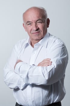 Confident senior man in white shirt crossing hands on chest and looking at camera while standing against gray background. Self confident senior isolated white studio shoot. photo