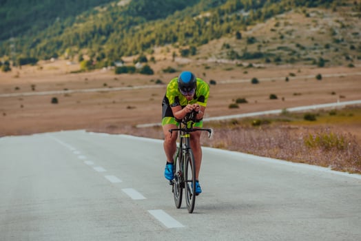 Full length portrait of an active triathlete in sportswear and with a protective helmet riding a bicycle. Selective focus photo